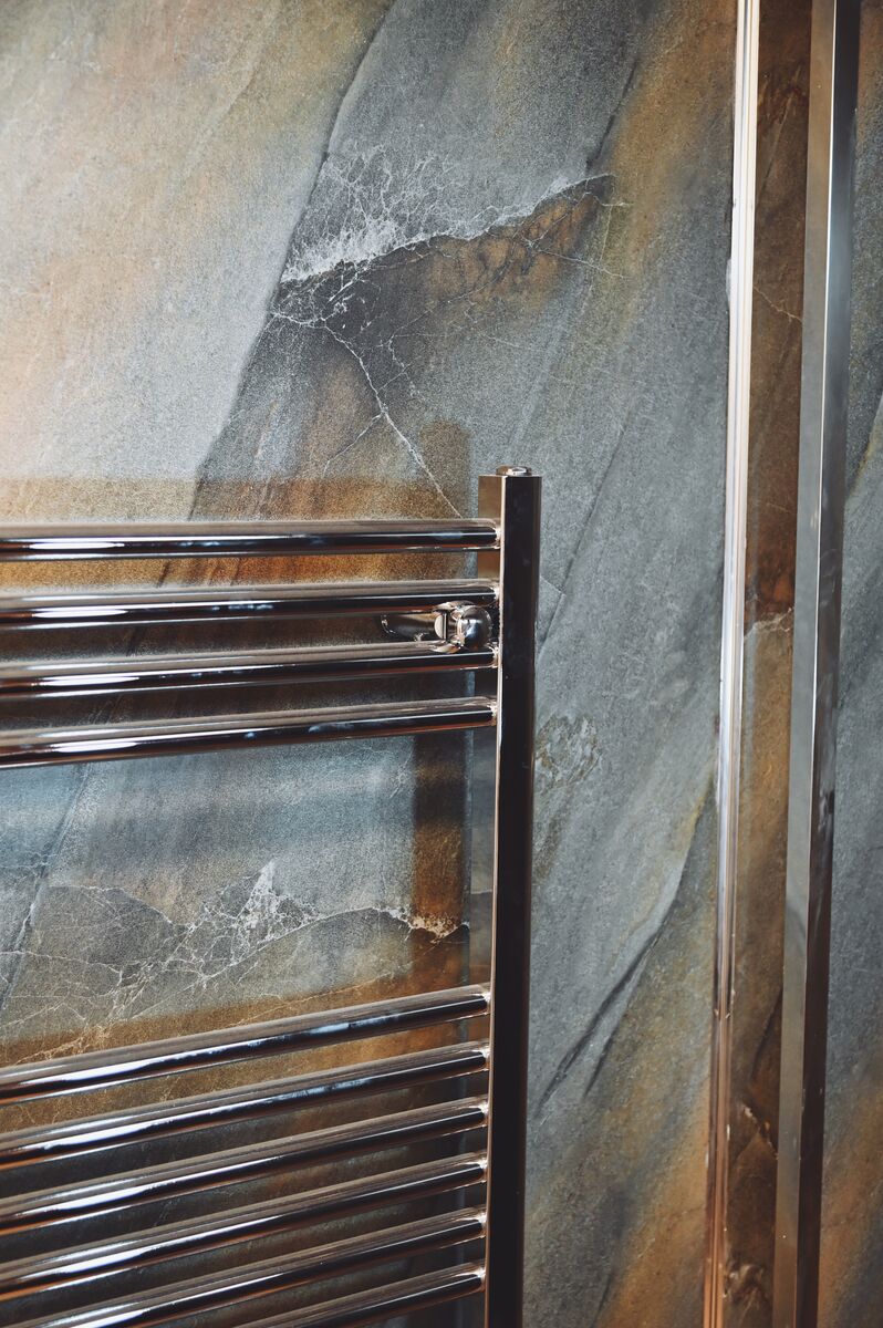 Chrome heated towel rail and marble-effect wall panels in a renovated bathroom